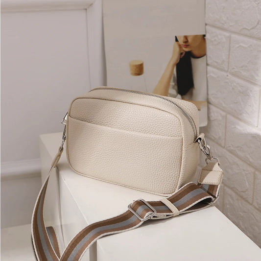 Beige textured handbag with a striped strap on a white surface