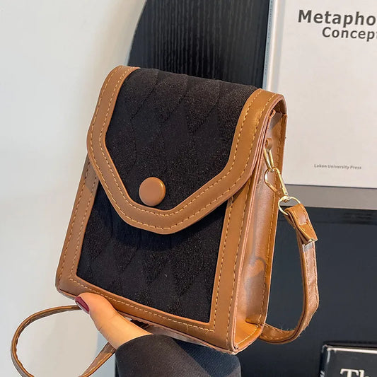 Black and brown crossbody bag held by a hand with a simple background