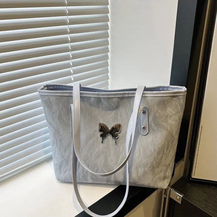 Blue tote bag with butterfly design on a surface near a window with blinds.