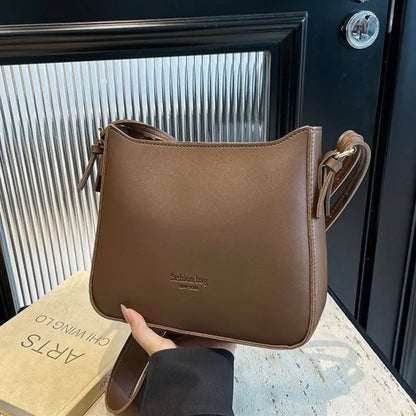 Brown shoulder bag held by a hand with a book in the background.