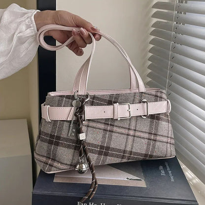 Handbag with plaid pattern and pink handle held by a hand, placed on a book.