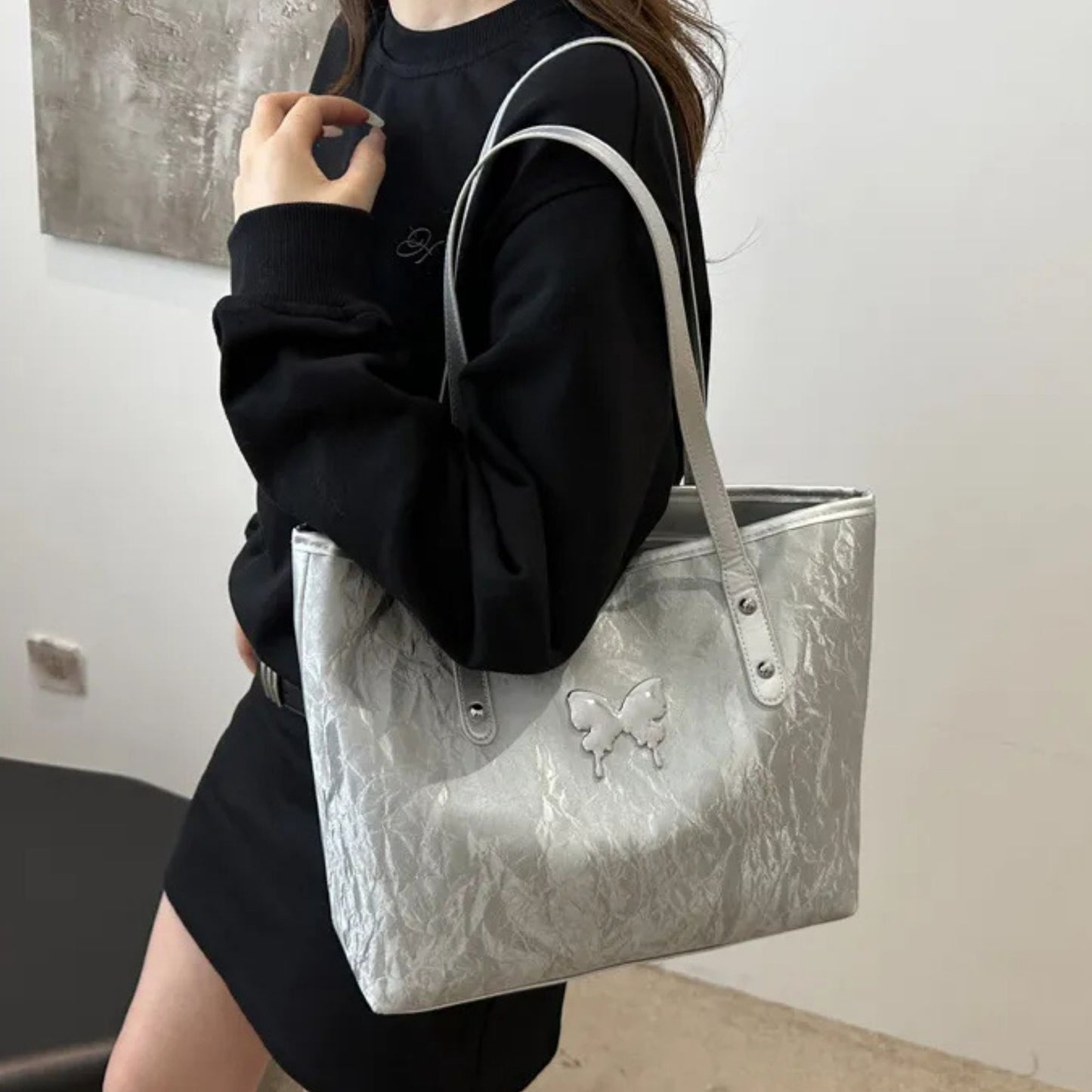 Person holding a silver textured totebag with a butterfly design.
