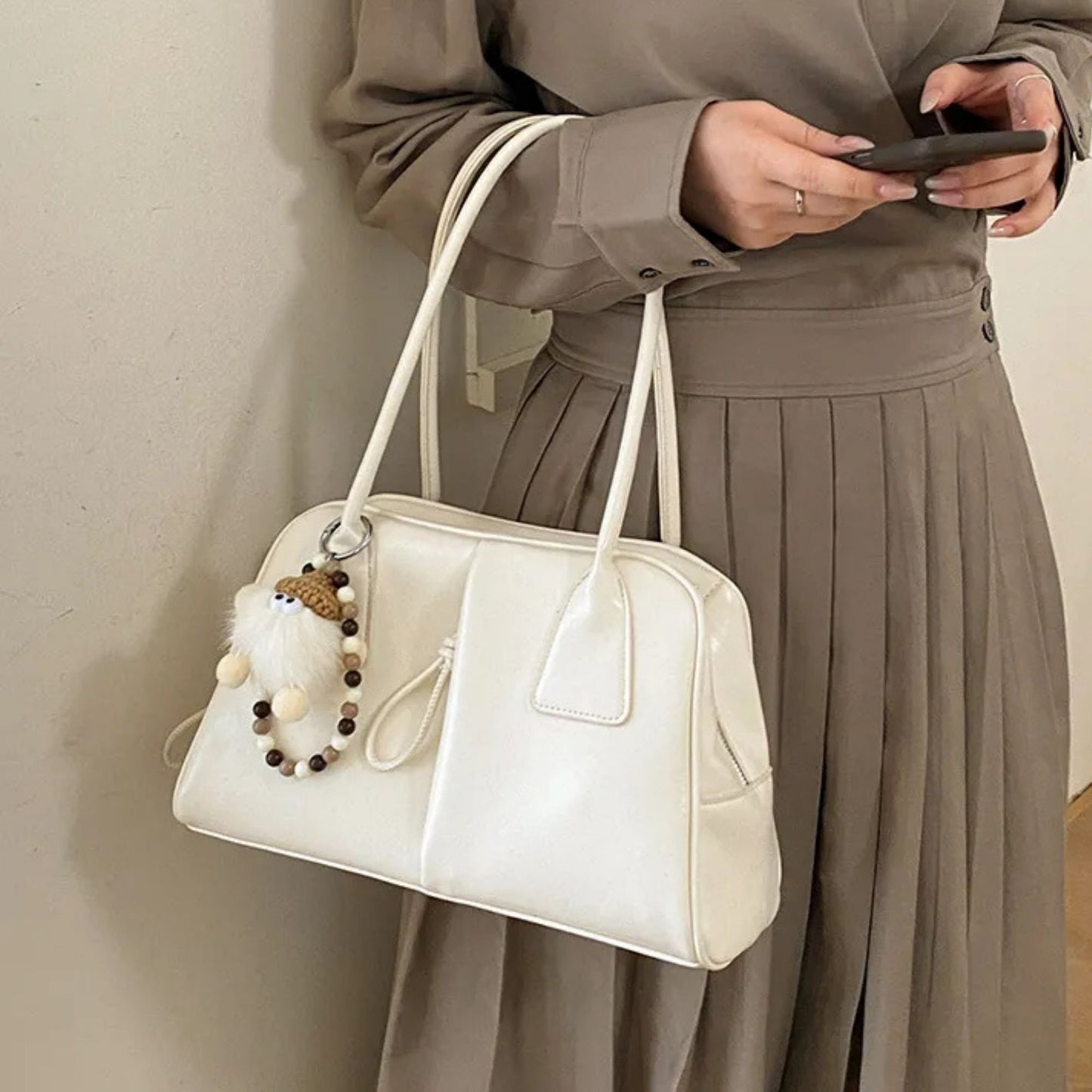 Person holding a white handbag with decorative elements against a neutral background