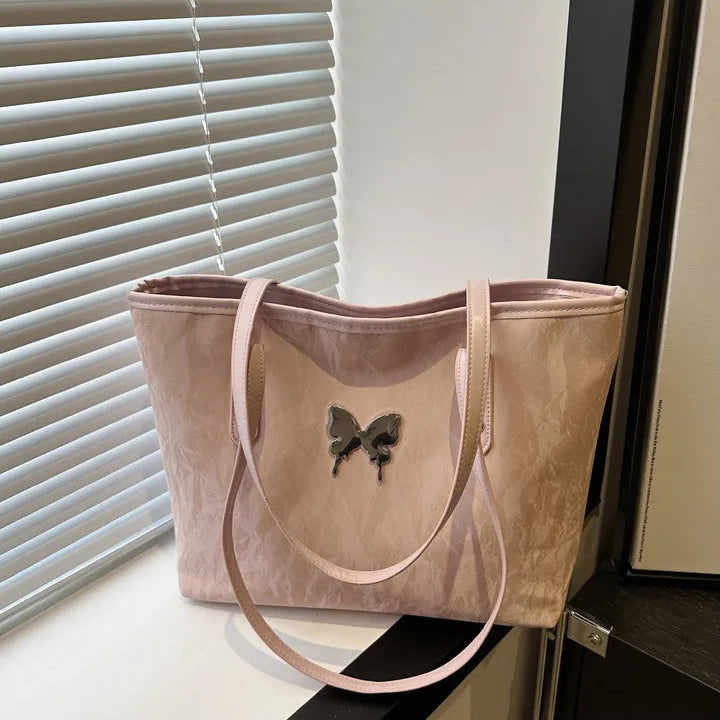 Pink tote bag with butterfly design on a surface near a window with blinds.