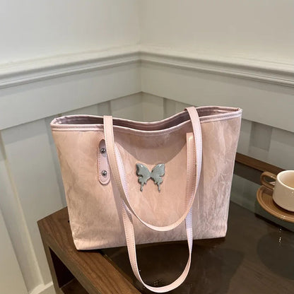 Pink tote bag with a butterfly charm on a wooden surface.