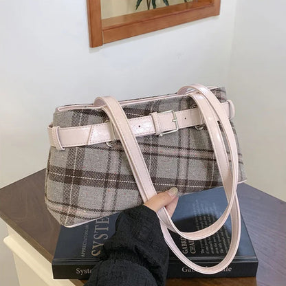 Plaid handbag with a pink strap held by a person on top of books.