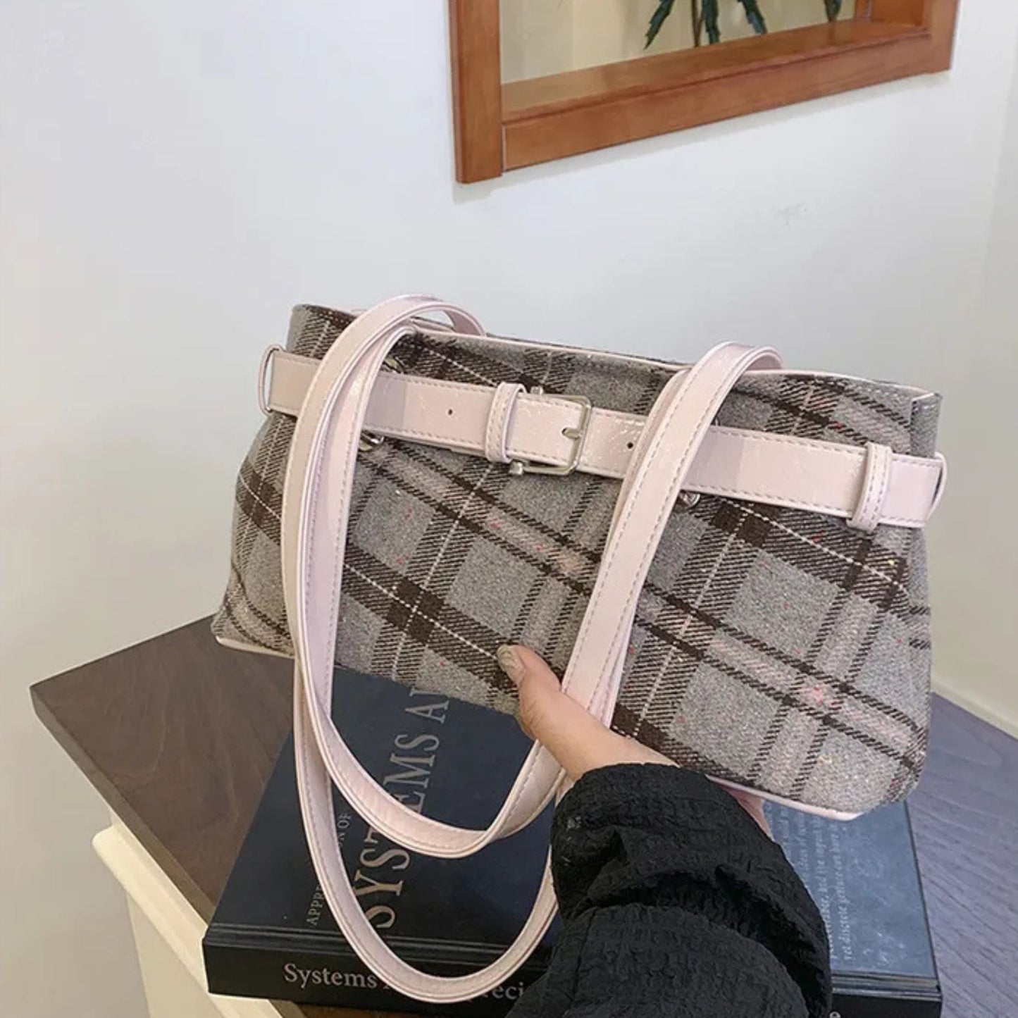 Plaid shoulder bag with a white strap held by a person on top of books.