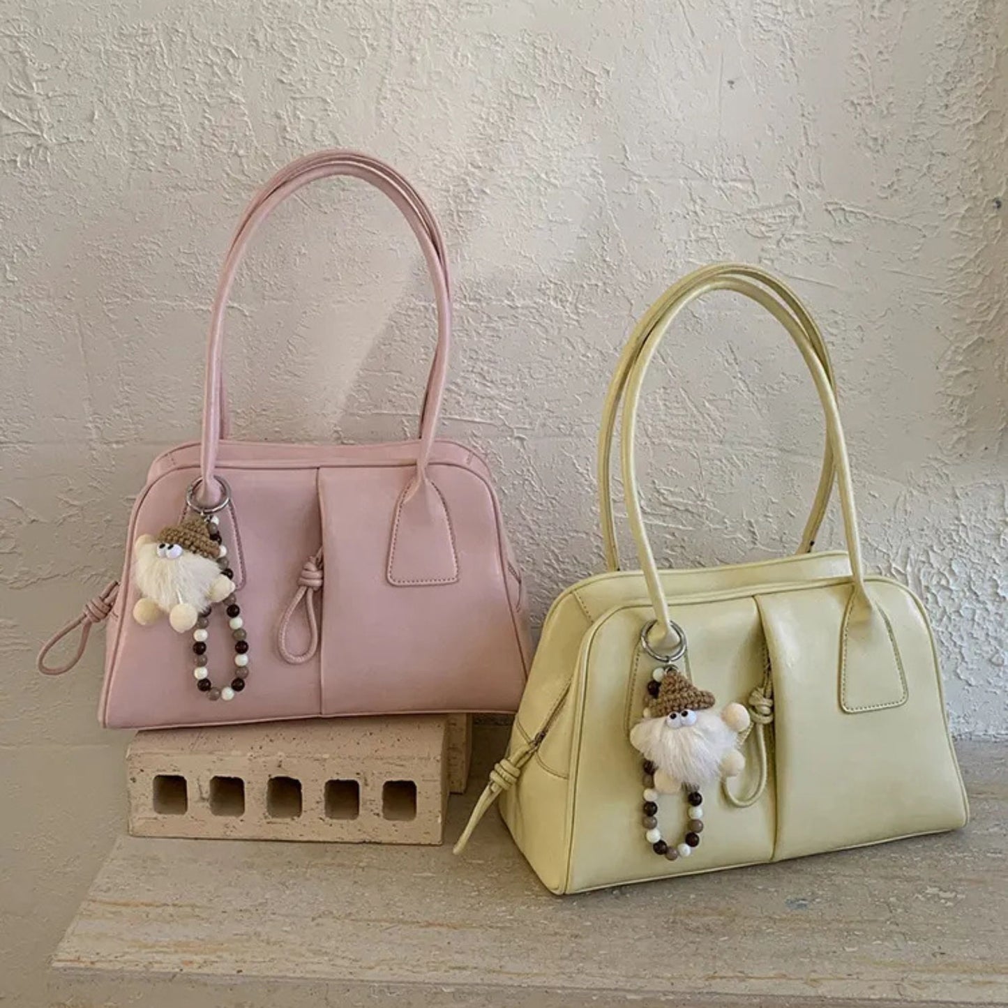 Two handbags, one pink and one yellow, with keychains on a textured surface.