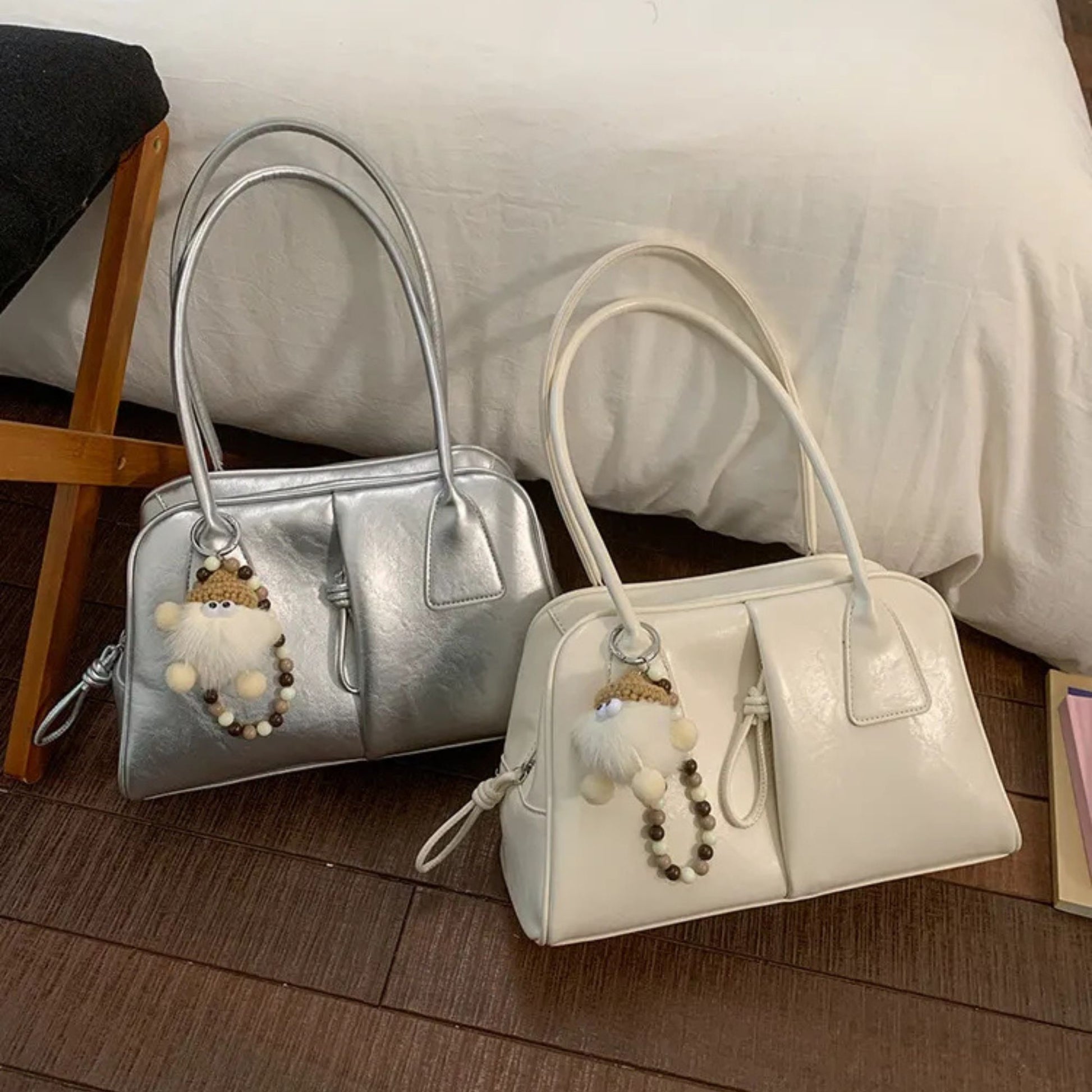 Two handbags, one silver and one white, with decorative charms on a wooden floor.