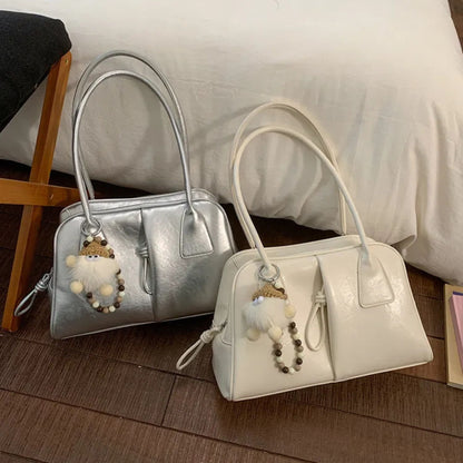 Two handbags, one silver and one white, with decorative charms on a wooden floor.