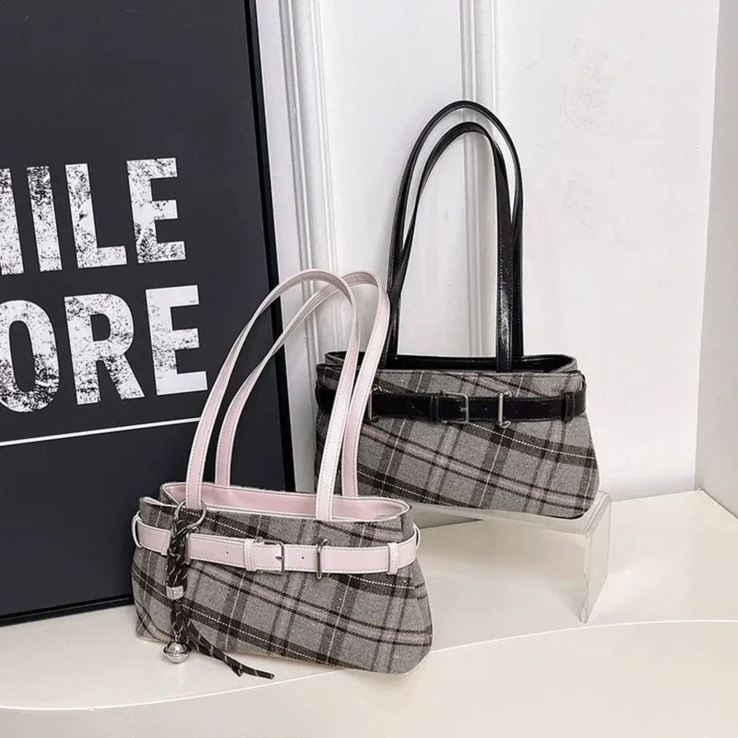 Two shoulder bags, one pink and one brown strap, on a white surface with a black and white background.