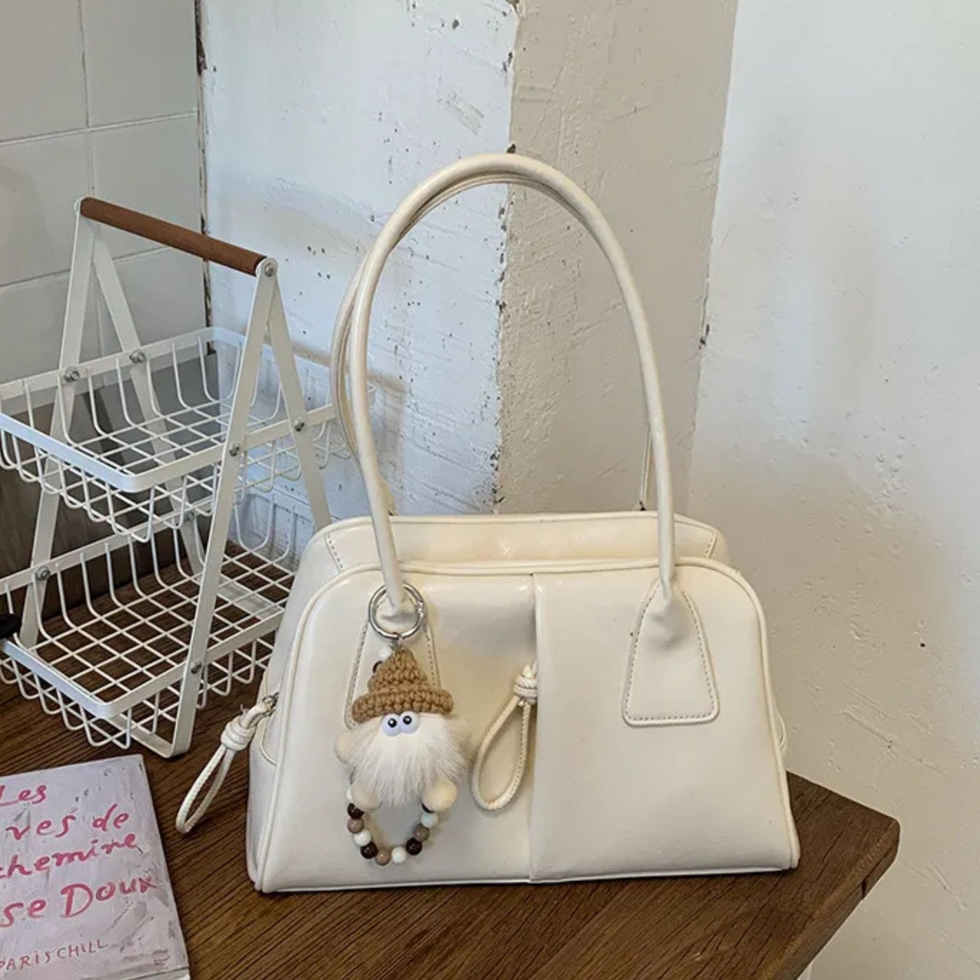 White handbag with a small gnome charm on a wooden surface.