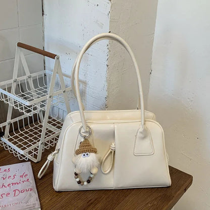 White handbag with a small gnome charm on a wooden surface.
