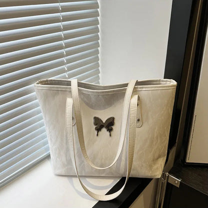 White tote bag with a butterfly design on a surface near a window with blinds.
