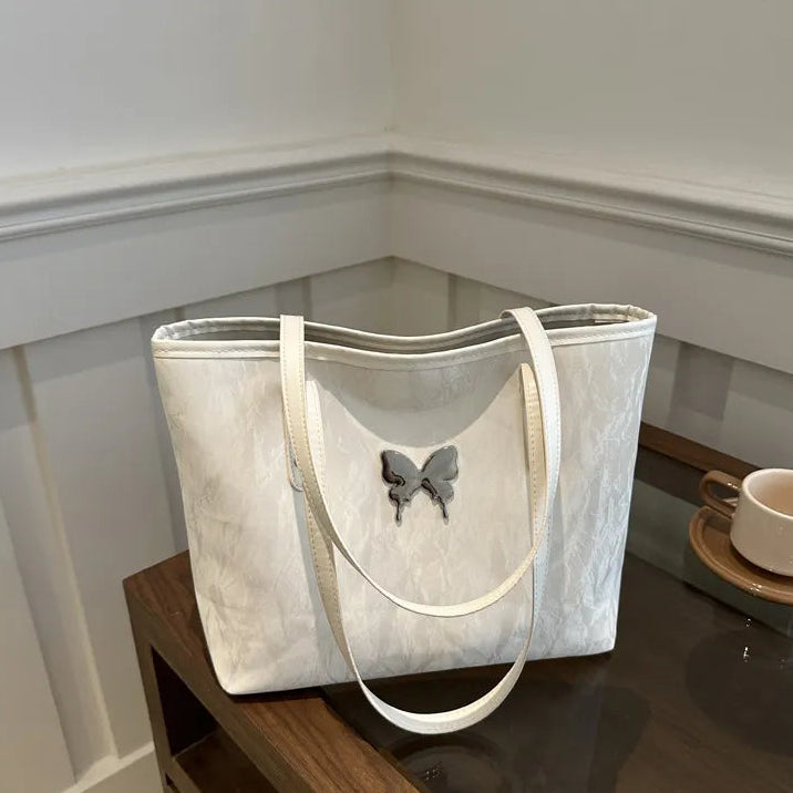 White tote bag with a butterfly design on a wooden surface.