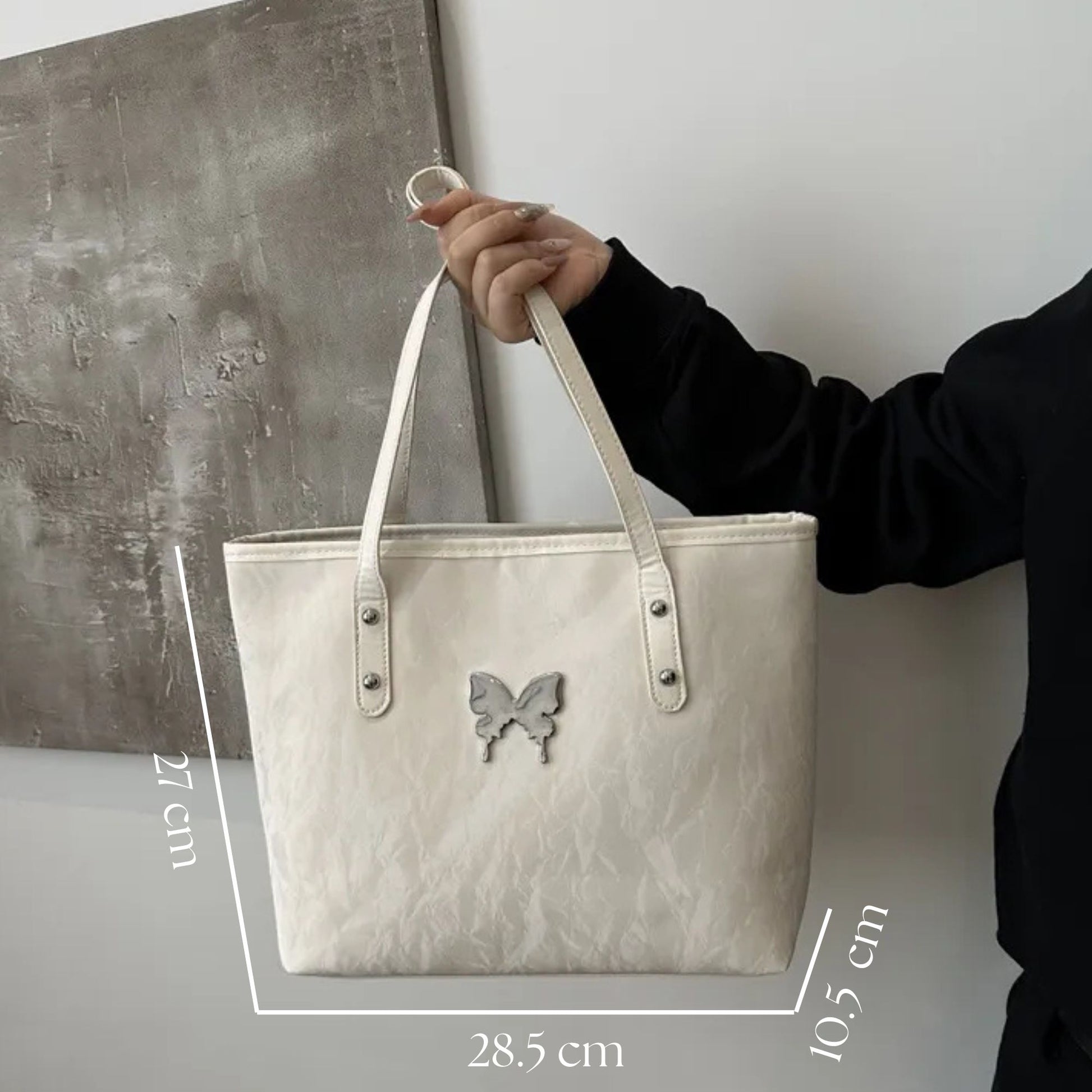 White tote bag with butterfly emblem held by a person, against a neutral background