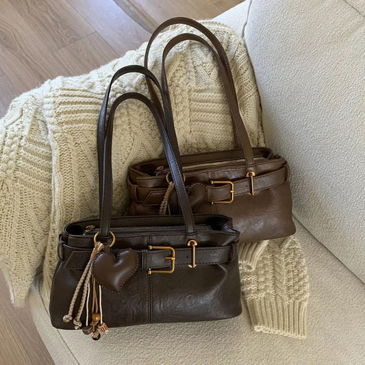Two brown shoulder bags on a textured surface with a beige knitted blanket.