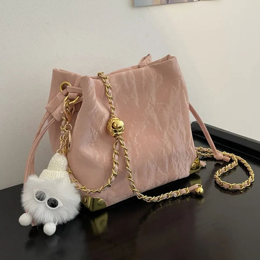 Pink bucket bag with gold chain and white fluffy keychain on a white walls background and brown surface