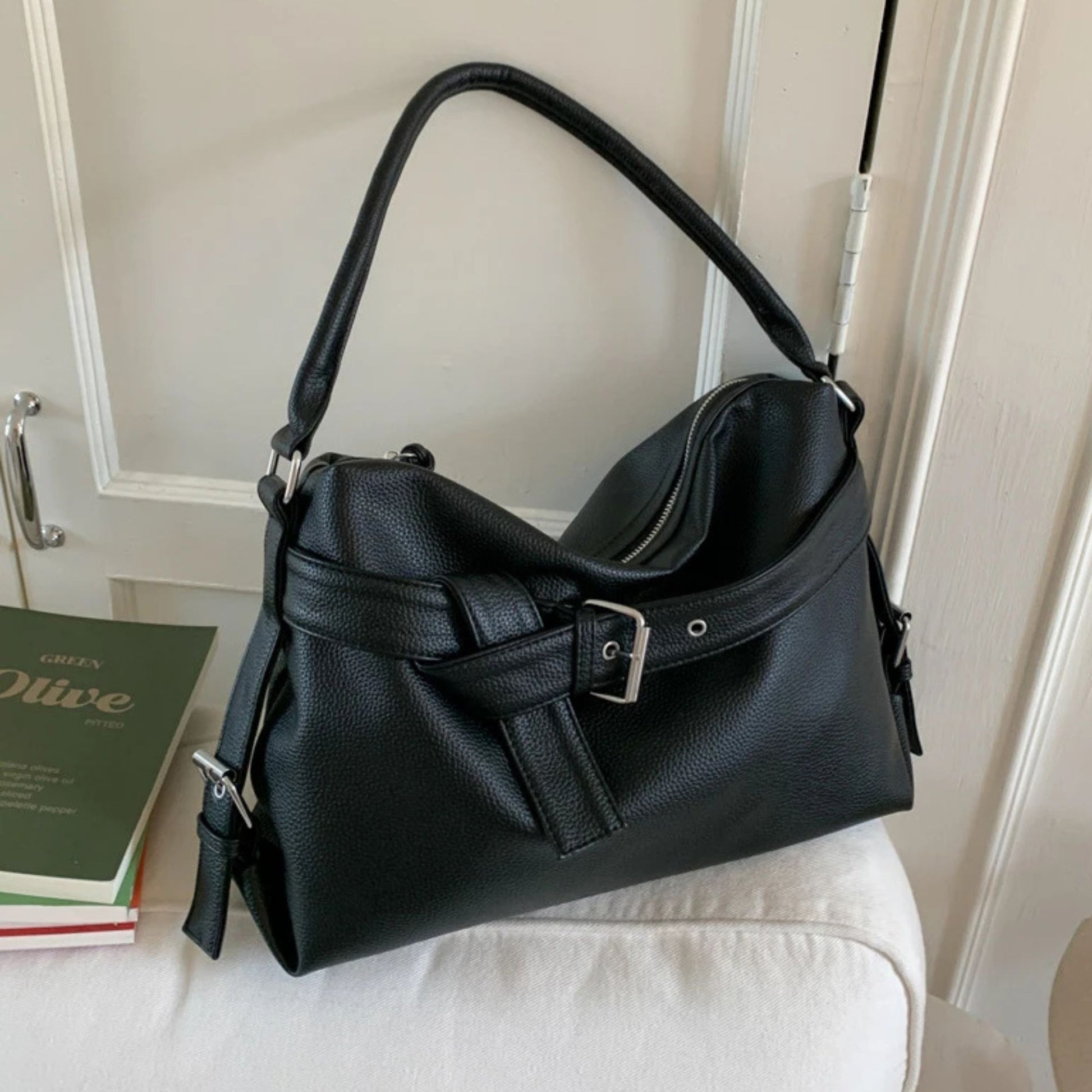 Black handbag on a white surface with a book in the background