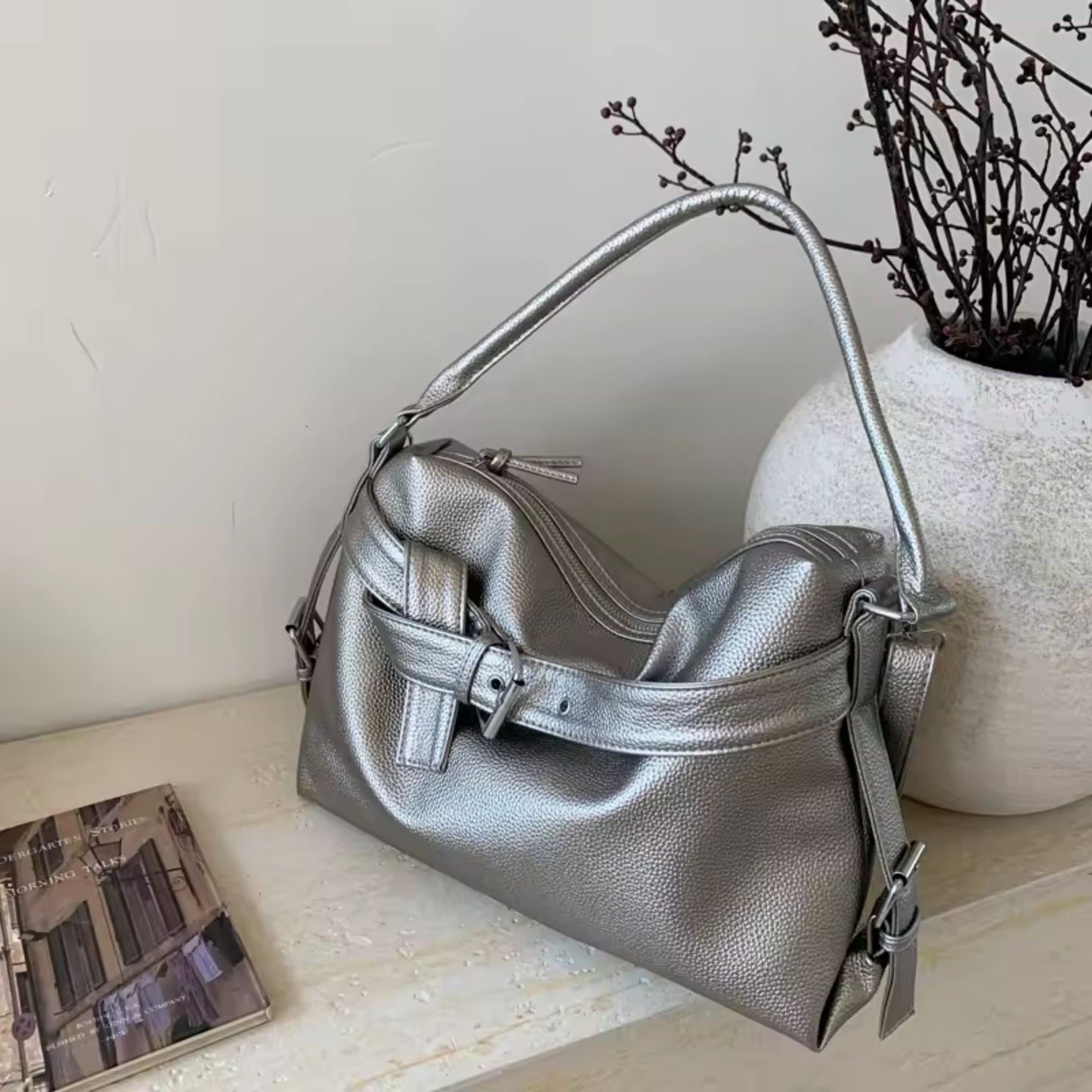 Silver large retro tote bag women on a light wooden surface with a vase and book in the background