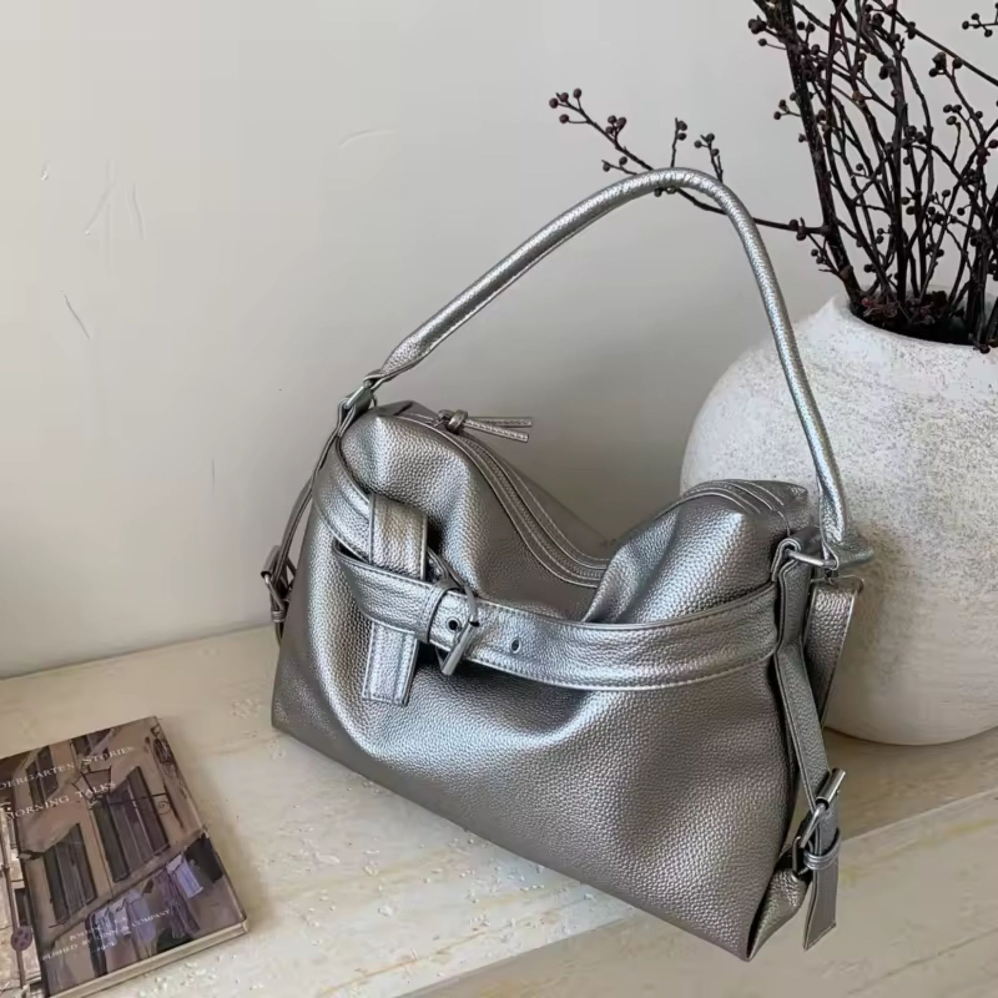 Silver large retro tote bag women on a light wooden surface with a vase and book in the background