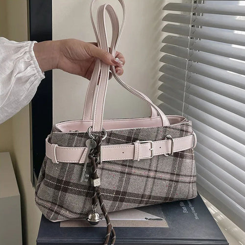 shoulder bag with plaid pattern and pink accents held by a hand, placed on a surface.
