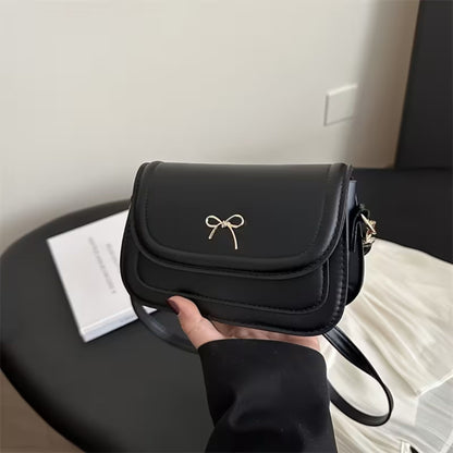 Black shoulder bag with a bow detail held by a person indoors.