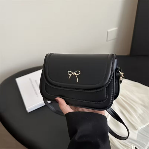 Black shoulder bag with a bow detail held by a person indoors.