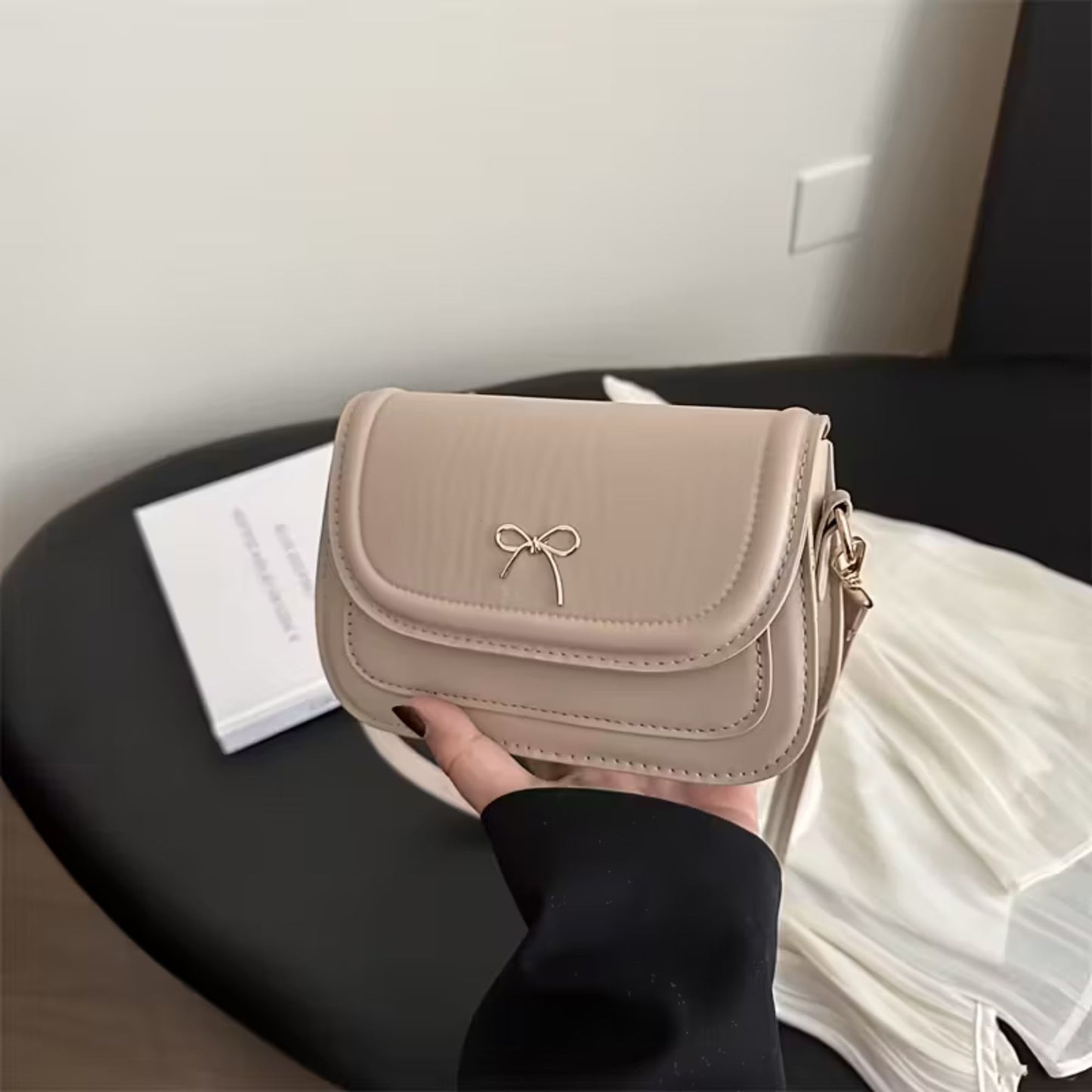 Beige shoulder bag with a bow detail held by a person in a casual setting.