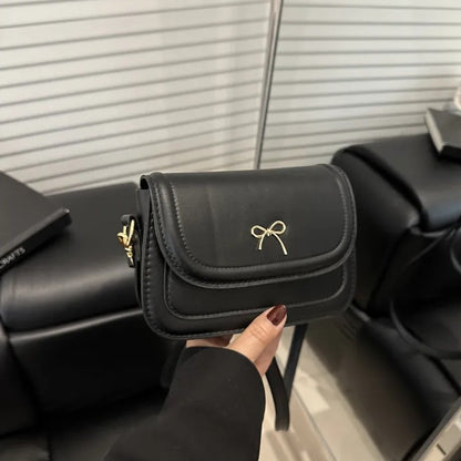 Black shoulder bag with a gold bow held by a person in indoor.