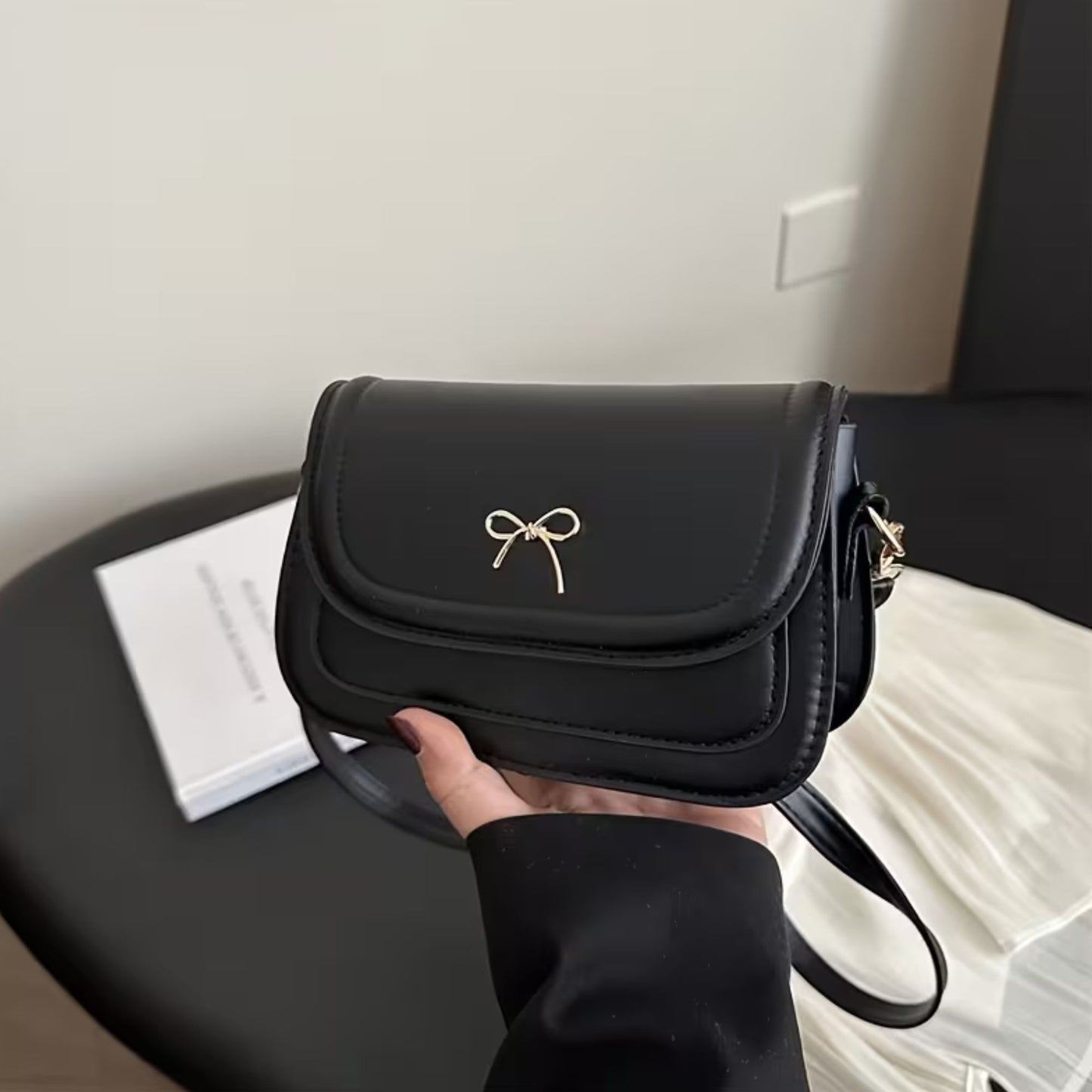 Black shoulder bag with a bow detail held by a person, placed on a surface.