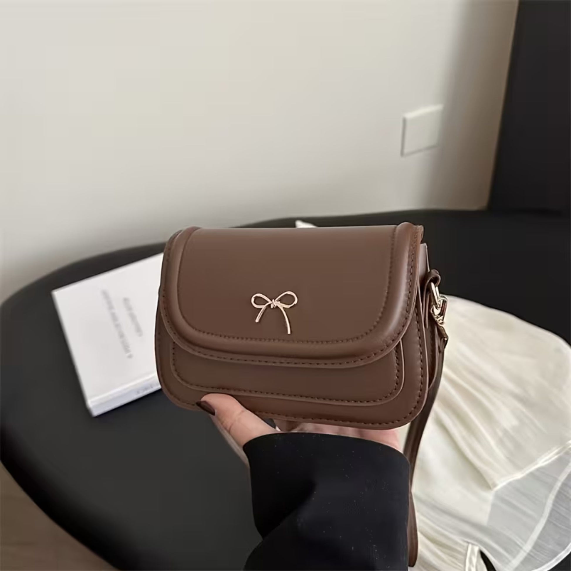 Brown shoulder bag with a bow detail held by a person in an indoor setting.