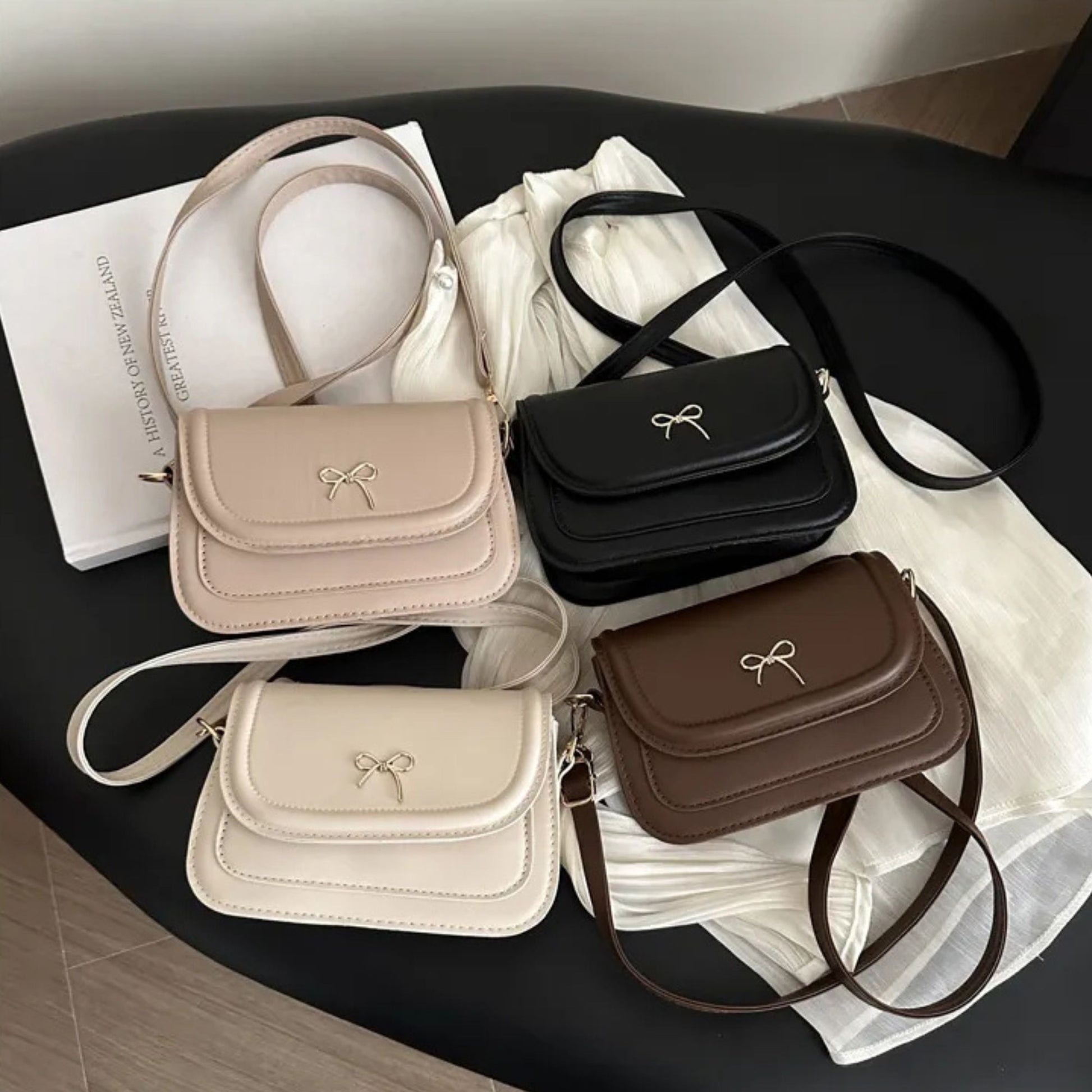 Four handbags in beige, black, white, and brown on a dark surface with a white cloth underneath.