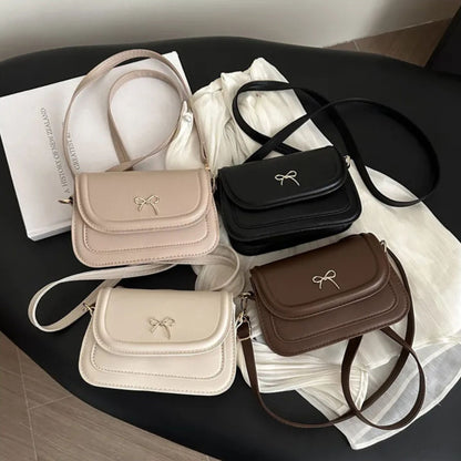Four handbags in beige, black, white, and brown on a dark surface with a white cloth underneath.