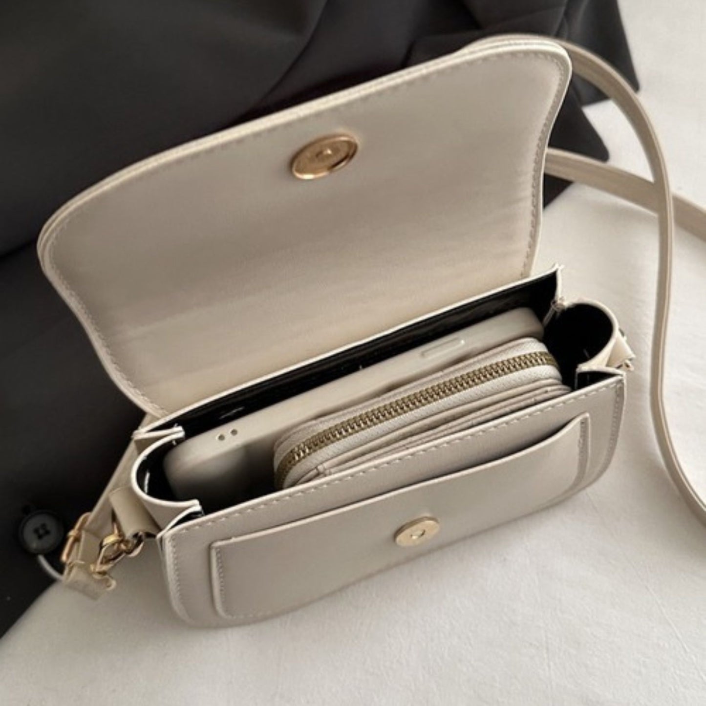 Beige shoulder bag with open compartment showing phone and wallet on a light surface.
