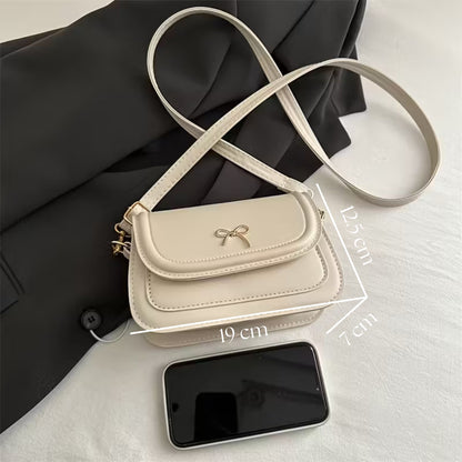 Beige handbag with a bow detail next to a smartphone on a light background with measurements