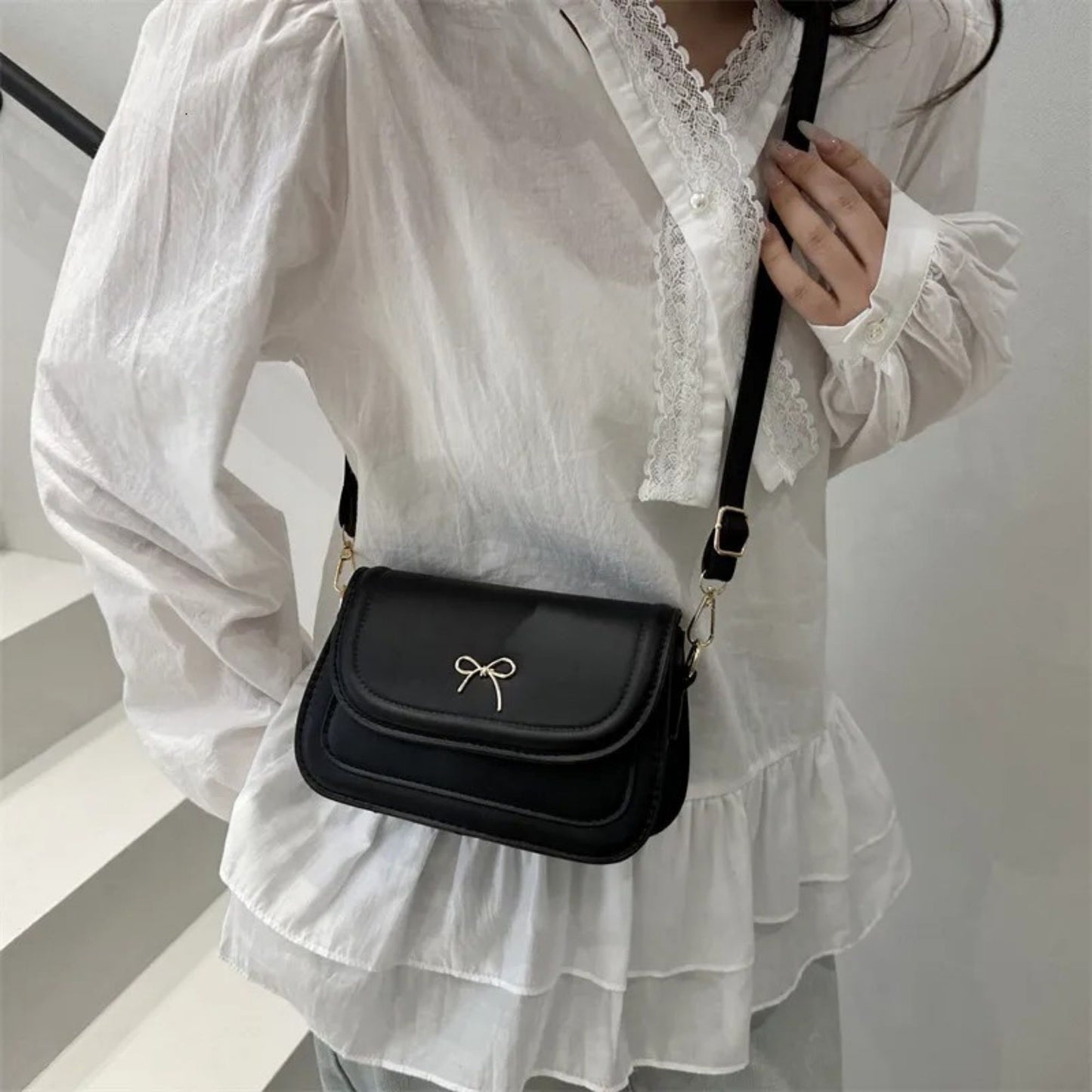 Person wearing a white blouse with lace details holding a black crossbody bag.
