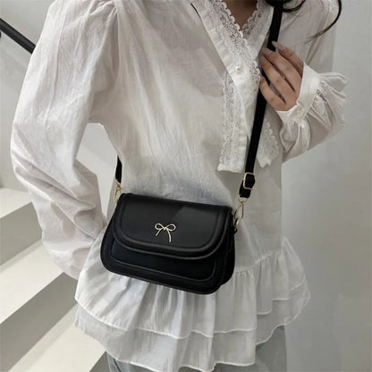Person wearing a white blouse with lace details holding a black crossbody bag.