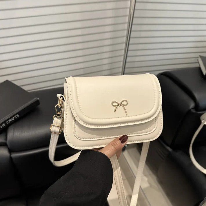 White shoulder bag with a bow detail held by a person in a black sleeve.