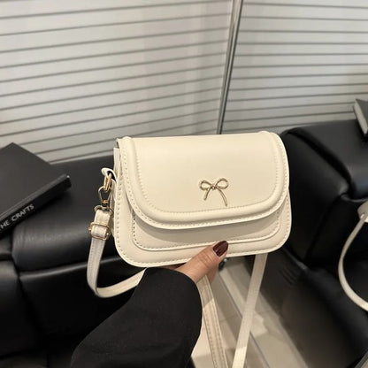 White shoulder bag with a bow detail held by a person in a black sleeve.
