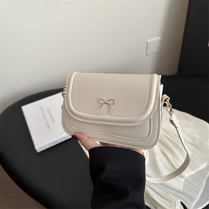 Beige shoulder bag with a bow detail held by a person, with a blurred background